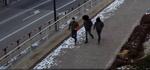 Młody mężczyzna idacy chodnikiem, obok niego dwóch innych.