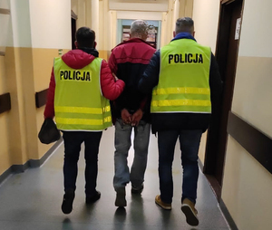 Dwóch policjantów prowadzi korytarzem zatrzymanego.