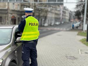 Dwaj policjanci drogówki wręczają mandat kierowcy samochodu osobowego, w tle przejście dla pieszych.