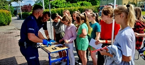 Policjanci na stoisku techniki kryminalistycznej, przed nimi grupa młodzieży szkolnej.