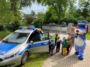 Policyjny radiowóz, policjant i dzieci przedszkolne.