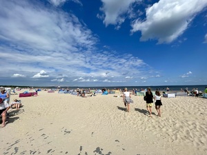 Plaża nadmorska a na niej wielu plażujących ludzi.