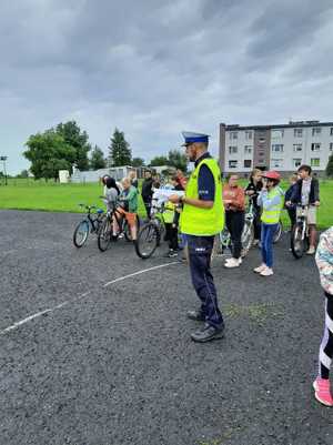 Policjant a za nim gromadka dzieci - uczestników egzaminu na kartę rowerową.