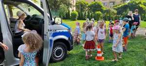 Po lewej radiowóz typu furgon i dzieci bawiące się wokół na trawniku