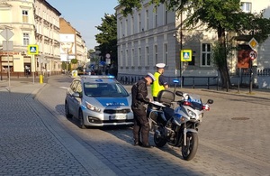 Policyjny radiowóz i policyjny motocykl, obok stoi policjant.