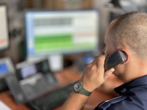 Policjant trzyma przy uchu słuchawkę, w tle monitory.