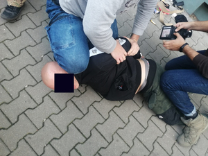 Dwóch policjantów po cywilnemu obezwładniło na chodniku podejrzanego - łysego mężczyznę. policjant po prawej przeszukuje jego rzeczy.