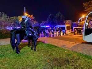 Zabezpieczenie meczu, po lewej dwaj policjanci na koniach, w tyle policjanci w szyku z tarczami.