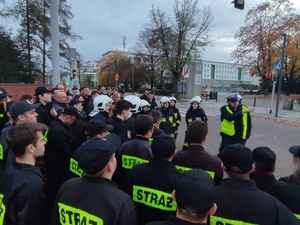 Grupa strażaków słucha wykładu policjanta drogówki.