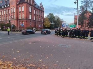 Policjant kieruje ruchem na skrzyżowaniu - obserwuje go grupa słuchaczy - strażaków.