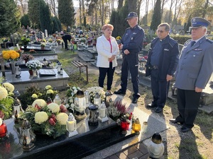 Cztery osoby stojące przy nagrobku. Od lewej - kobieta - matka zmarłego policjanta, komendant miejski, kapelan policji i szef stowarzyszenia emerytów.