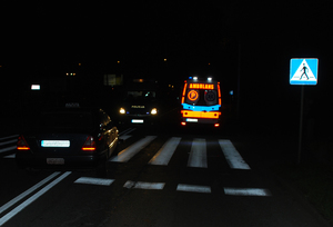 Na zdjęciu widzimy - nocne zdjęcie przejścia dla pieszych na którym stoją samochód osobowy, dalej radiowóz policyjny i karetka pogotowia.