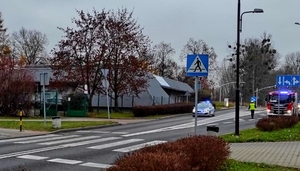 Na zdjęciu widzimy przejście dla pieszych a w tle na ulicy po lewej policyjny radiowóz, po prawej wóz strażacki. Widać postać policjanta.