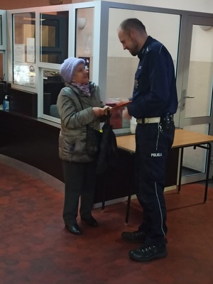 Na zdjęciu policjant przekazuje odblask seniorce.