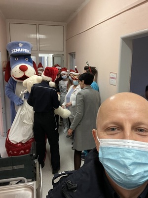 Na zdjęciu widzimy personel szpitalny, policjantkę i policyjną maskotkę - Psa Sznupka. oraz twarz rzecznika policji gliwickiej robiącego tzw. zdjęcie selfie.