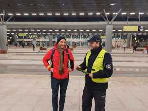 Policjant wręcza odblask mężczyźnie stojącemu w centrum przesiadkowym