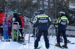 Na zdjęciu dwaj policjanci na stoku narciarskim - maja na nogach narty, na głowach kaski