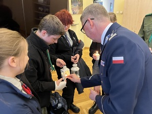 Na zdjęciu komendant pochyla się nad przyniesionym przez harcerzy światłem - świecą.