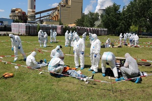 Na zdjęciach trawnik a na nim kilkadziesiąt osób w kombinezonach, w tle jakiś zakład przemysłowy.