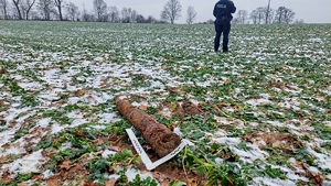 Na zdjęciu skorodowany pocisk artyleryjski oraz linijka techników kryminalistyki. W tle policjant.