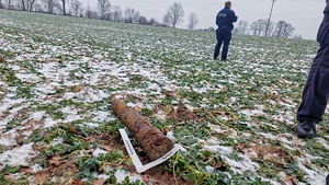 Na zdjęciu skorodowany pocisk artyleryjski oraz linijka techników kryminalistyki. W tle policjant.