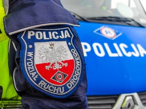 Ozdobna tarcza na rękawie munduru policjanta - z napisem wydział ruchu drogowego, w tle radiowóz