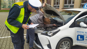 Na zdjęciu widać, jak policjant wraz z uczestnikiem konkursu zagląda pod maskę pojazdu.