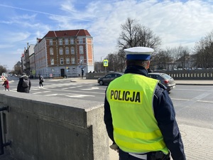 Na zdjęciu policjant patrzący na ulicę i znajdujące się tam przejście dla pieszych.