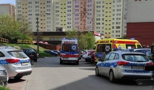 Na fotografii osiedlowa uliczna. Widać zaparkowane samochody w tym dwie karetki pogotowia i dwa radiowozy.