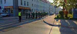 Na zdjęciu widzimy ulicę, którą maszeruje  orkiestra dęta, z nimi policjant.