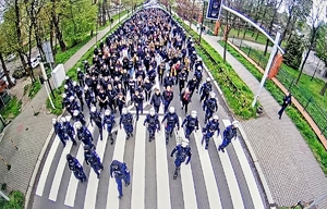 Na zdjęciu widzimy tłum kibiców idących ulica prowadzonych w eskorcie policji.