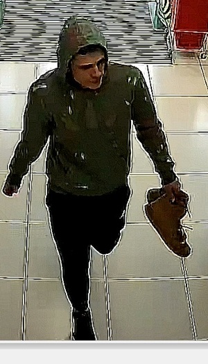 Na zdjęciu młody mężczyzna idący z parą butów w lewej dłoni.