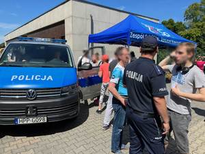 Na zdjęciu widzimy policjanta rozmawiającego z uczniem. po lewej widać radiowóz i młodzież oglądająca jego wnętrze.