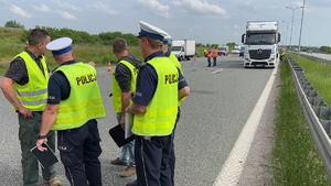 Grypa policjantów po lewej w tle samochód ciężarowy i autostrada.