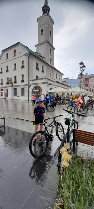 Zdjęcie przedstawia metę rajdu na gliwickim rynku. Na pierwszym planie widać chłopca w wieku szkolnym z rowerem, a w oddali widać coraz to większą ilość dojeżdżających kolaży.