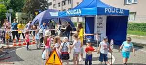 Zdjęcie przedstawia imprezę pod nazwą „Bezpieczne wakacje młodych gliwiczan”, na pierwszym planie widzimy namioty Policji i Straży Miejskiej oraz grupy dzieci przedszkolnych, wykonujących różne zadania. Grupa pod namiotem policyjny wysłuchuje pogadanki, a pod namiotem Straży Miejskiej trenuje refleks na specjalnym urządzeniu.