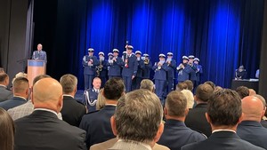Na zdjęciu scena na której stoi policjant laktor a obok policyjna orkiestra - widać licznych widzów.