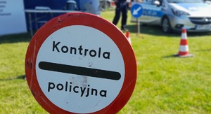 Na zdjęciu widzimy znak drogowy - kontrola policji, który jest ustawiony na trawniku.