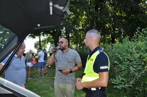 Zdjęcie z pikniku policyjnego, zrobione na terenach zielonych przy Klubie Garnizonowym w Gliwicach, na pierwszym planie widzimy jak umundurowany policjant przeprowadza kontrolę trzeźwości mężczyzny.