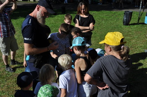 Zdjęcie z pikniku policyjnego, zrobione na terenach zielonych przy Klubie Garnizonowym w Gliwicach, na pierwszym planie widzimy umundurowanego policjanta z psem policyjnym, który jest otoczony dziećmi.