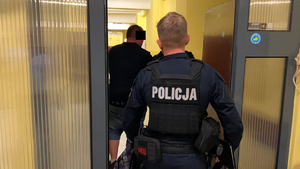 Policjanci prowadzą podejrzanego korytarzem, przechodzą przez drzwi