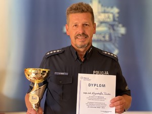 Aspirant Krzysztof Tacka pozuje, trzymając w prawej ręce puchar, w lewej - dyplom.