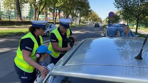 Na zdjęciu po lewej dwoje policjantów i uczeń szkoły podstawowej stoi przy kontrolowanym samochodzie osobowym.