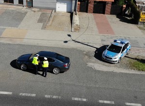 Kontrola drogowa na ulicy. Widać dwoje policjantów kontrolujących auto typu sedan