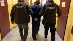 Na zdjęciu dwóch policjantów prowadzi zatrzymanego podejrzanego o zabójstwo.