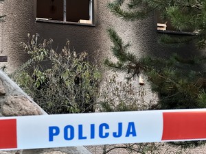 Na zdjęciu policyjna taśmia z napisem POLICJA, w tle okno spalonej plebanii.