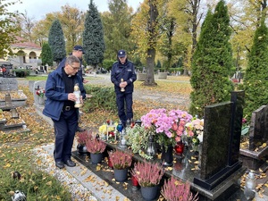 Na zdjęciu widzimy kapelana policji oraz dwóch oficerów stojących w zadumie przy nagrobku. Kapelan stawia znicz na nagrobku.