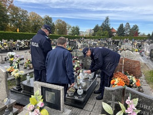 Na zdjęciu widzimy kapelana policji oraz oficerów stojących w zadumie przy nagrobku. Jeden z oficerów stawia znicz na nagrobku.