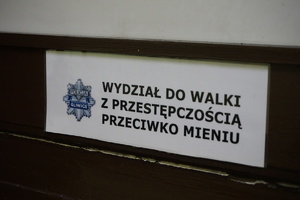 Na zdjęciu plakietka drzwiowa z napisem wydział do walki z przestępczością przeciwko mieniu.