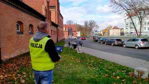 Na zdjęciu policjant operator drona stoi ptzy ulicy. w tle ulica, wysoko dron.